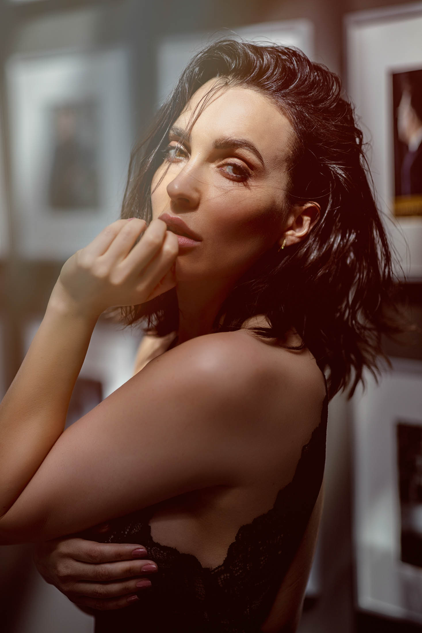 Eine brünette Frau mit elegantem Make-up und einem schwarzen Spitzentop blickt nachdenklich nach oben und stützt ihr Kinn in einer warm beleuchteten künstlerischen Umgebung auf ihre Finger. © Fotografie Tomas Rodriguez