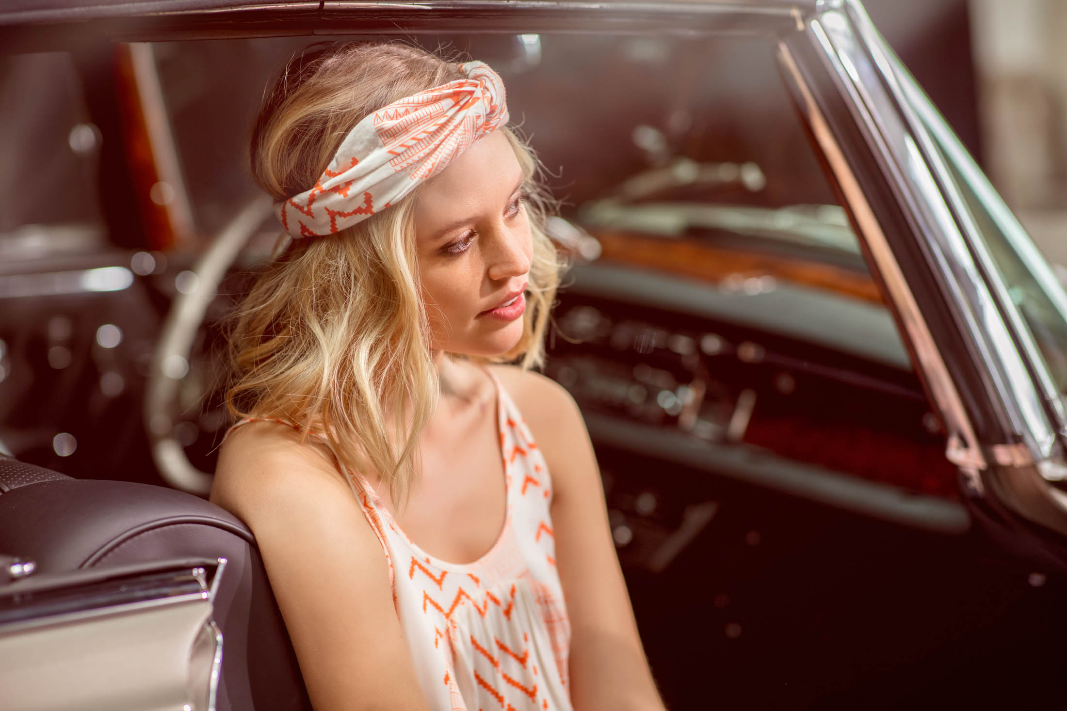 Eine junge Frau mit Stirnband blickt nachdenklich, während sie auf dem Fahrersitz eines Oldtimers sitzt, dessen Innenraum einsehbar ist. © Fotografie Tomas Rodriguez