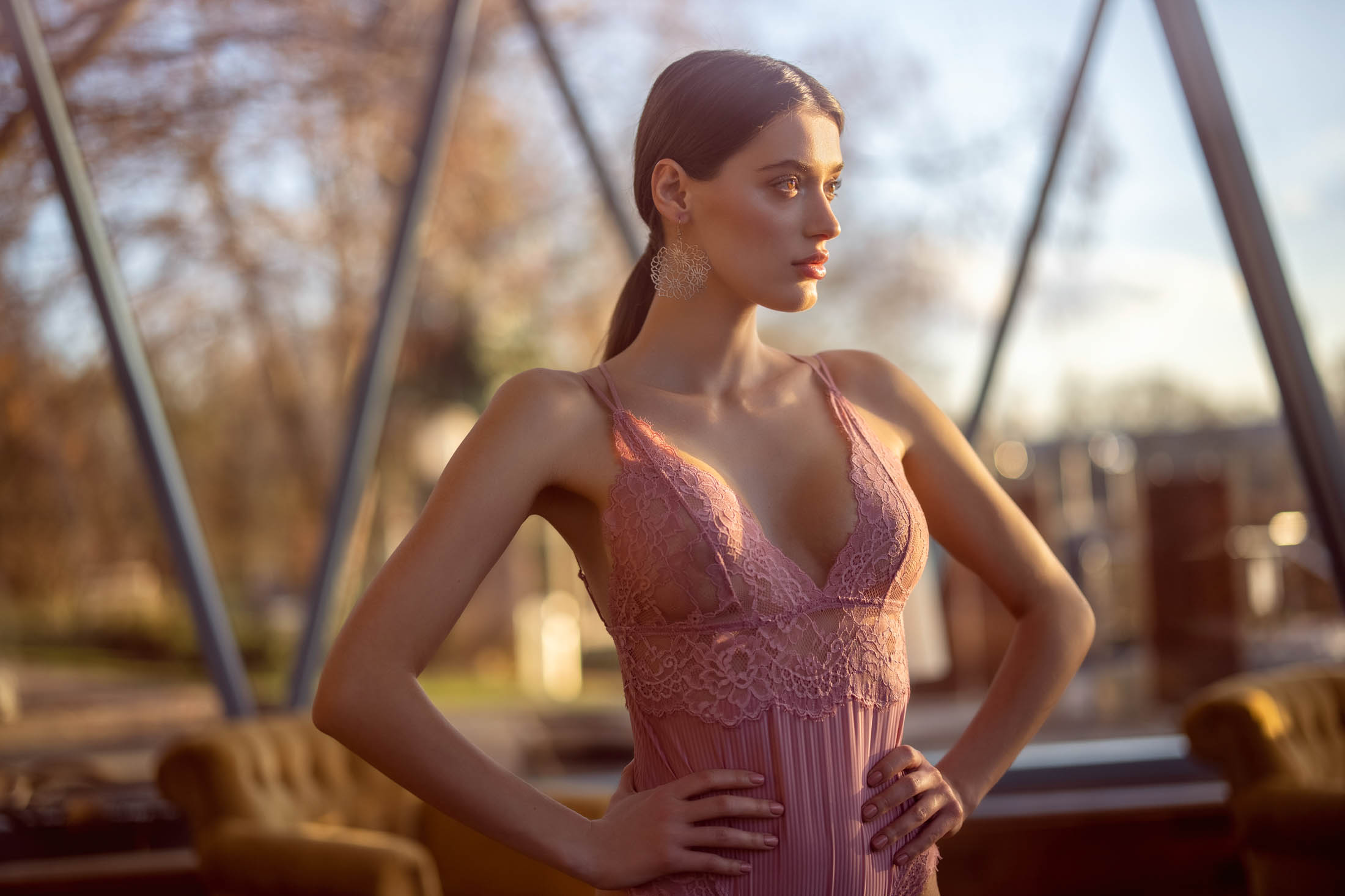 Eine Frau in einem eleganten rosa Spitzenkleid steht bei Sonnenuntergang in einem Park, wobei das sanfte Sonnenlicht ihren ruhigen Gesichtsausdruck und ihr Profil hervorhebt. © Fotografie Tomas Rodriguez