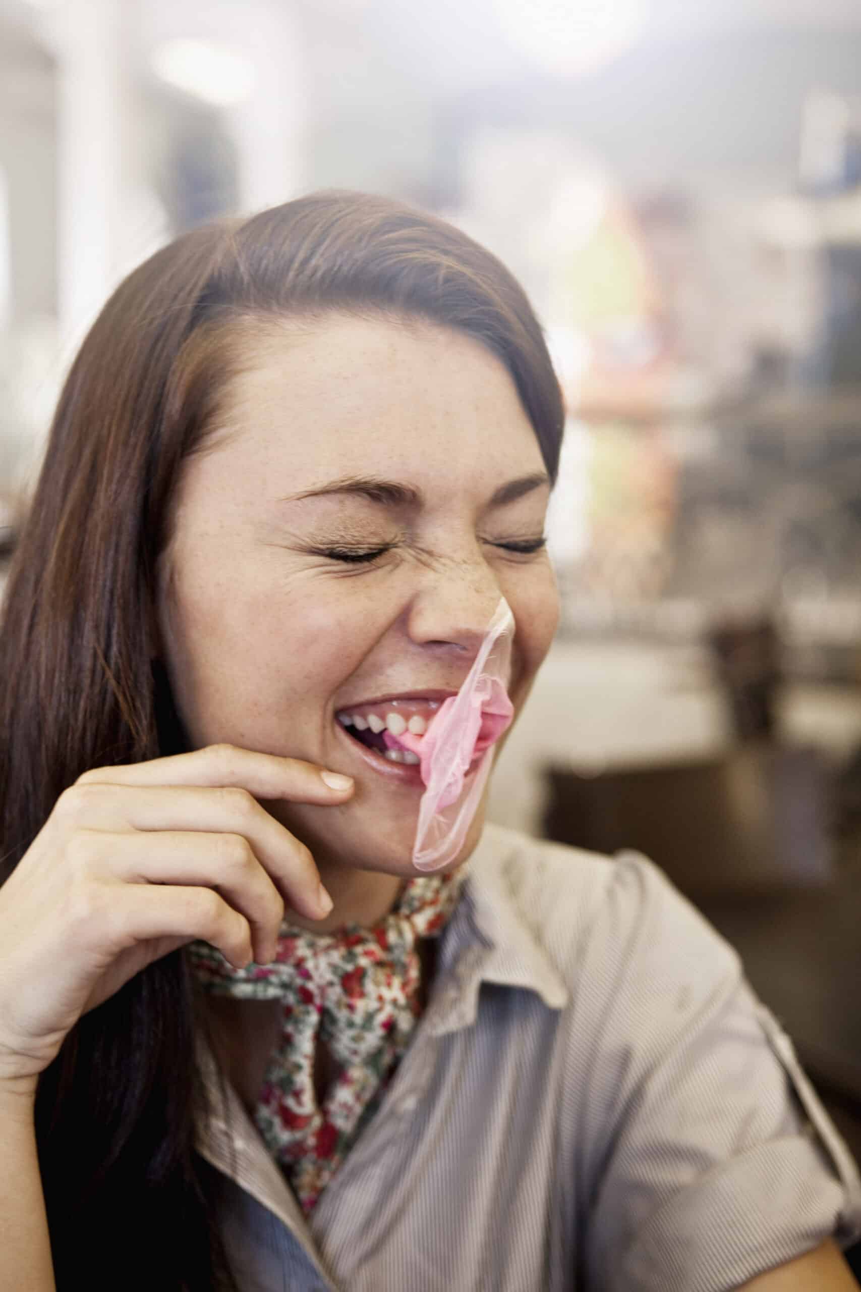 Eine fröhliche junge Frau mit langen braunen Haaren, die in einer Diner-ähnlichen Umgebung lacht und ein Stück rosa Kaugummi aus ihrem Mund zieht. © Fotografie Tomas Rodriguez