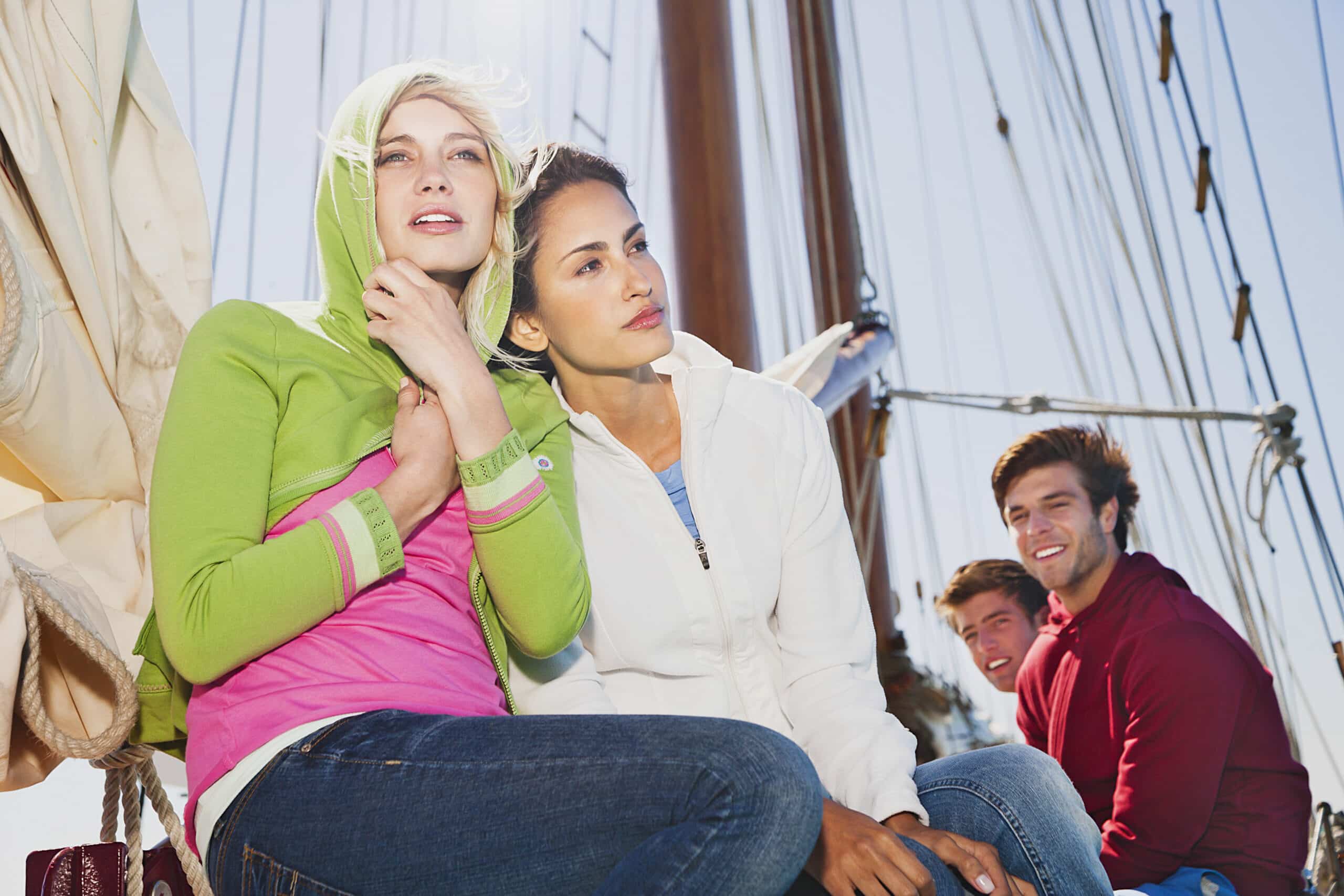 Vier Personen sitzen auf einem Segelboot und genießen einen sonnigen Tag. Zwei Frauen im Vordergrund tragen legere Jacken und Jeans, eine trägt einen grünen Kapuzenpullover, die andere eine weiße. Zwei Männer im Hintergrund tragen ebenfalls legere Kleidung. Segel und Takelage sind sichtbar. © Fotografie Tomas Rodriguez