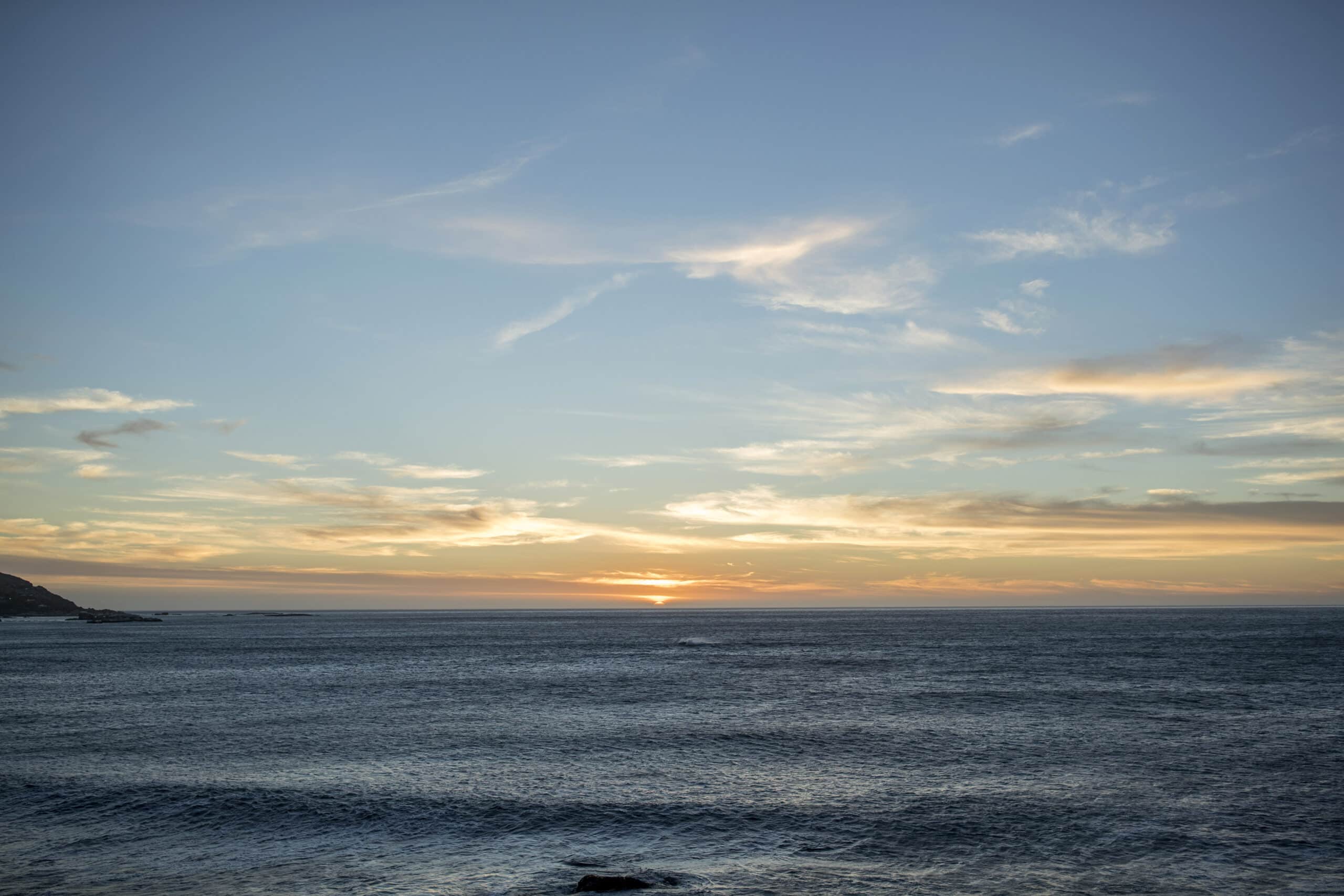Ein ruhiger Sonnenuntergang über dem Ozean mit vereinzelten Wolken und ruhiger See und sanften Blau- und Orangetönen am Himmel. © Fotografie Tomas Rodriguez