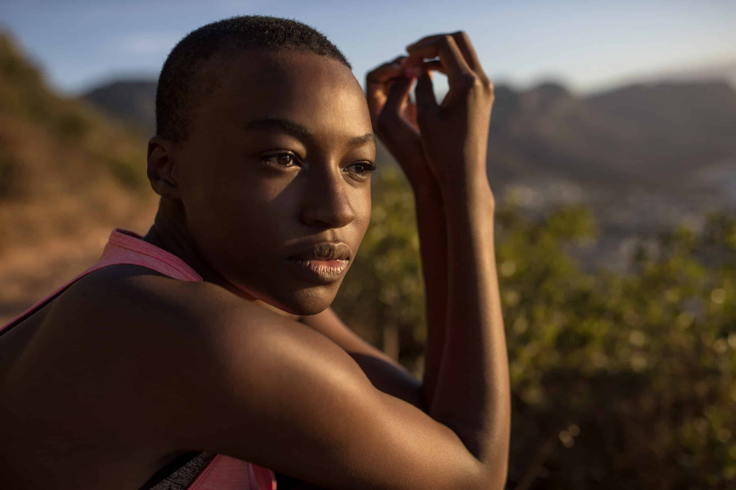 Eine junge schwarze Frau mit konzentriertem Gesichtsausdruck streckt ihren Arm im Freien aus, im Hintergrund ist eine in sanftes Sonnenuntergangslicht getauchte Berglandschaft zu sehen. © Fotografie Tomas Rodriguez