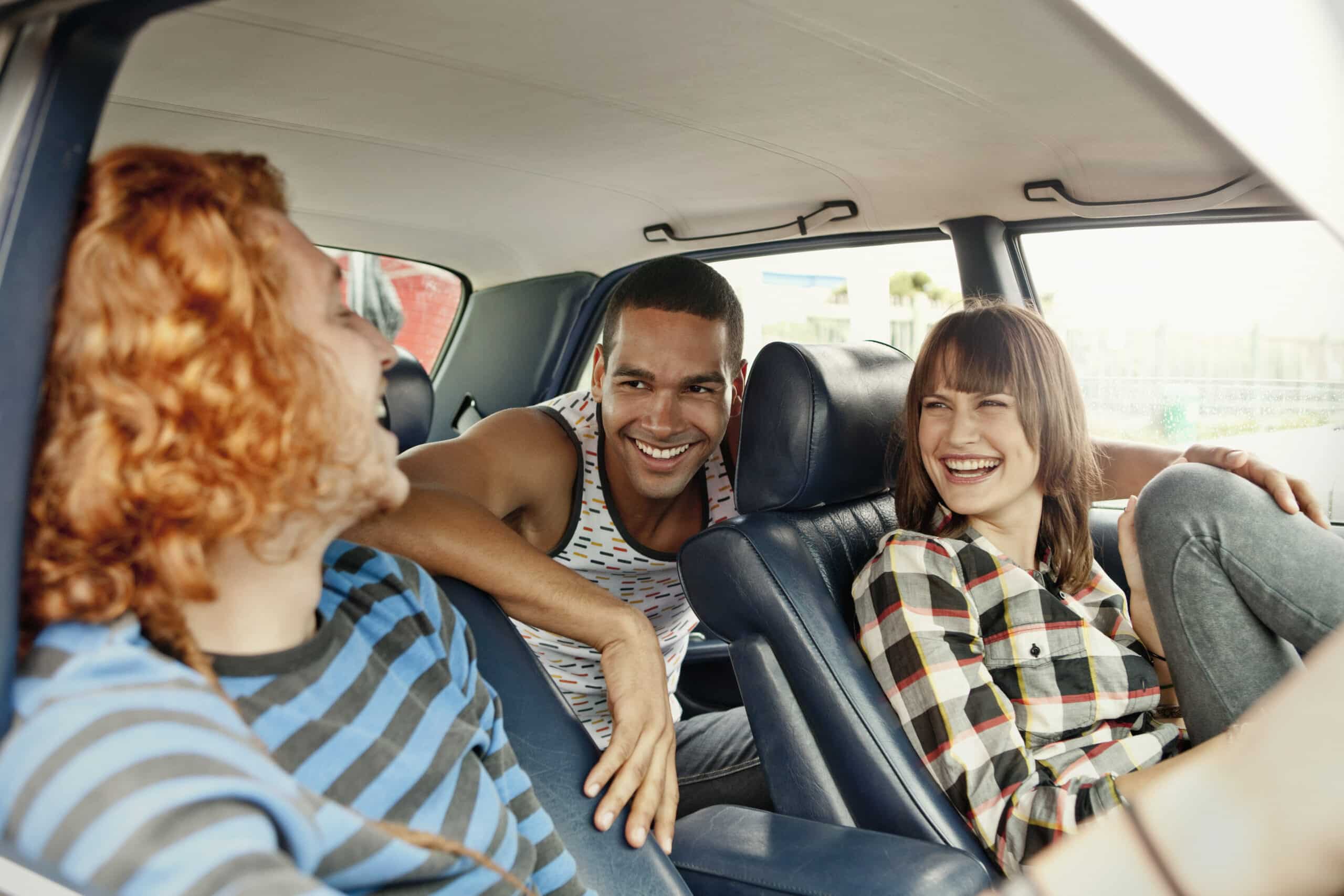 Drei Freunde genießen einen Roadtrip. Das Bild zeigt sie in einem Auto. Die rothaarige Person im gestreiften Hemd sitzt auf dem Vordersitz, ihr gegenüber sitzen zwei lächelnde Freunde, einer im Tanktop, der andere im karierten Hemd, auf dem Rücksitz. Sie scheinen alle eine gute Zeit zu haben. © Fotografie Tomas Rodriguez