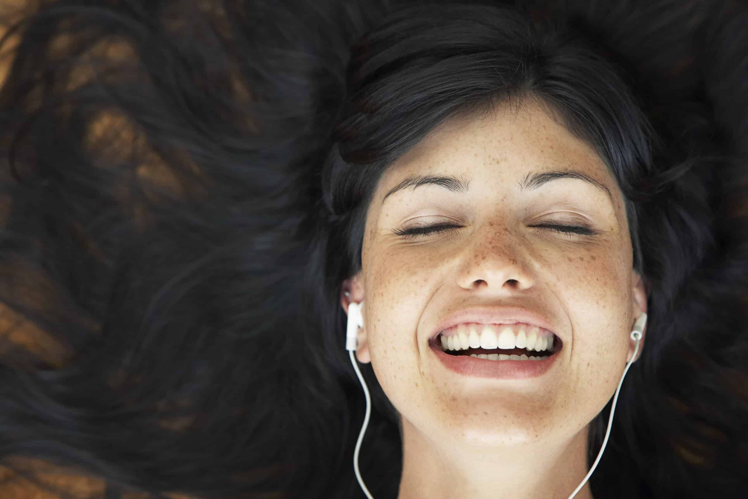 Nahaufnahme einer Person mit dunklem Haar, die liegt, lächelt und die Augen geschlossen hat, während sie über Kopfhörer Musik hört. © Fotografie Tomas Rodriguez