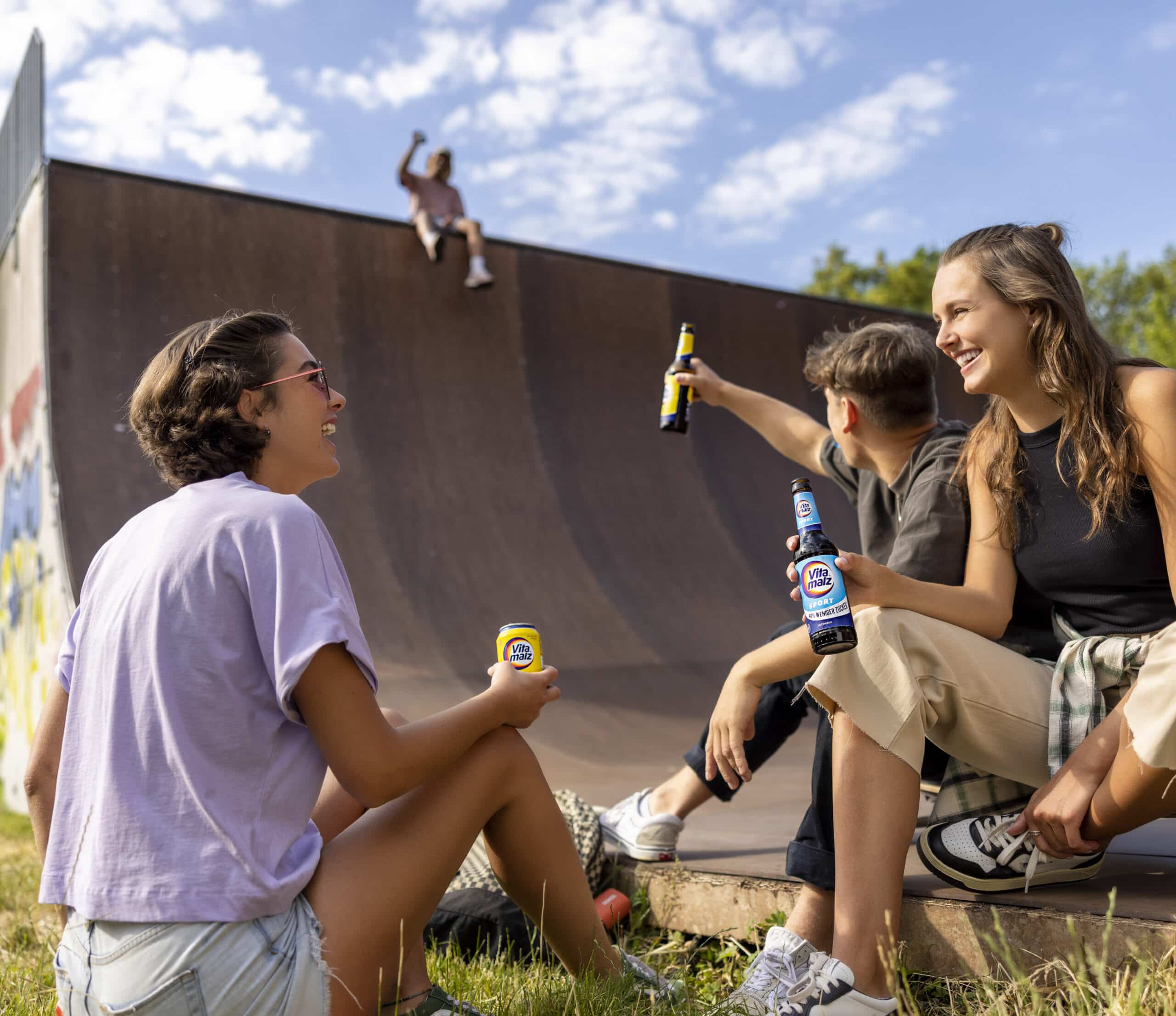 Vier junge Erwachsene sitzen bei sonnigem Wetter entspannt an einer Skaterampe, halten Bierflaschen in den Händen und lachen. Einer sitzt oben auf der Rampe, hält eine Bierflasche in den Händen und hebt den Arm. Die Szene wirkt fröhlich und lässig. © Fotografie Tomas Rodriguez