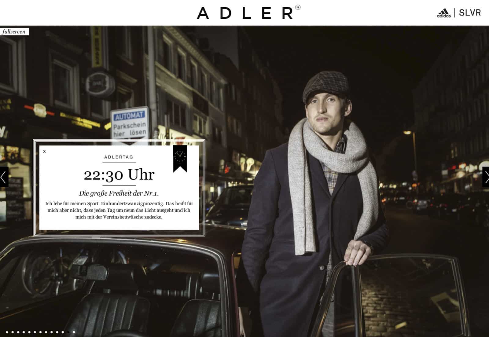 Ein stilvoll gekleideter Mann steht selbstbewusst nachts auf einer Stadtstraße neben einem geparkten Auto. Er ist warm angezogen mit Mantel, Schal und Schiebermütze. Oben im Bild ist das ADLER-Logo zu sehen, links von ihm erscheint ein Textfeld mit der Uhrzeit „22:30 Uhr“ und einer deutschen Beschriftung. © Fotografie Tomas Rodriguez
