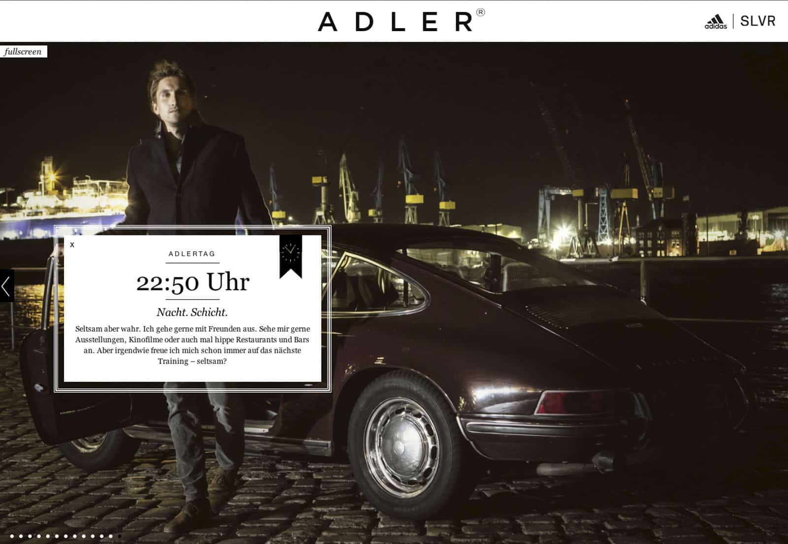 Ein Mann steht neben einem Oldtimer, der nachts auf einer Kopfsteinpflasterstraße geparkt ist. Im Hintergrund sind ein Industriehafen und beleuchtete Kräne zu sehen. Der Text auf dem Bild lautet oben „ADLER“ und enthält die Uhrzeit „22:50 Uhr“, gefolgt von einem Absatz auf Deutsch, der mit „Schon...“ beginnt. © Fotografie Tomas Rodriguez