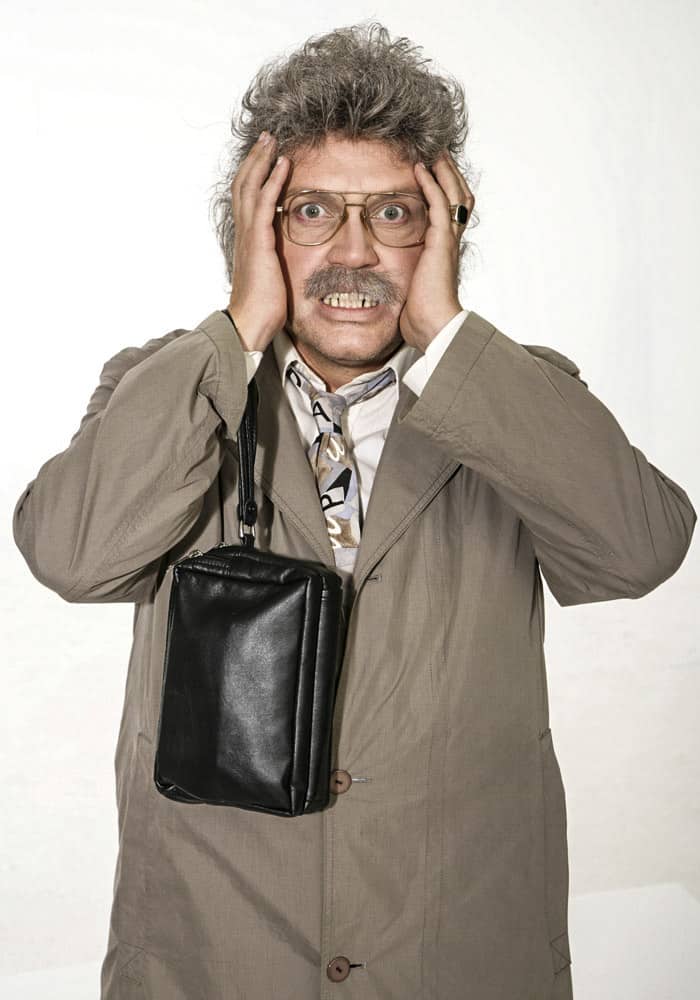 Ein Mann mit überraschtem Gesichtsausdruck steht mit den Händen auf dem Kopf. Er hat graue Haare, eine Brille und einen Schnurrbart. Er trägt eine beige Jacke, eine gemusterte Krawatte und eine schwarze Tasche hängt über seiner Schulter. Der Hintergrund ist schlicht weiß. © Fotografie Tomas Rodriguez