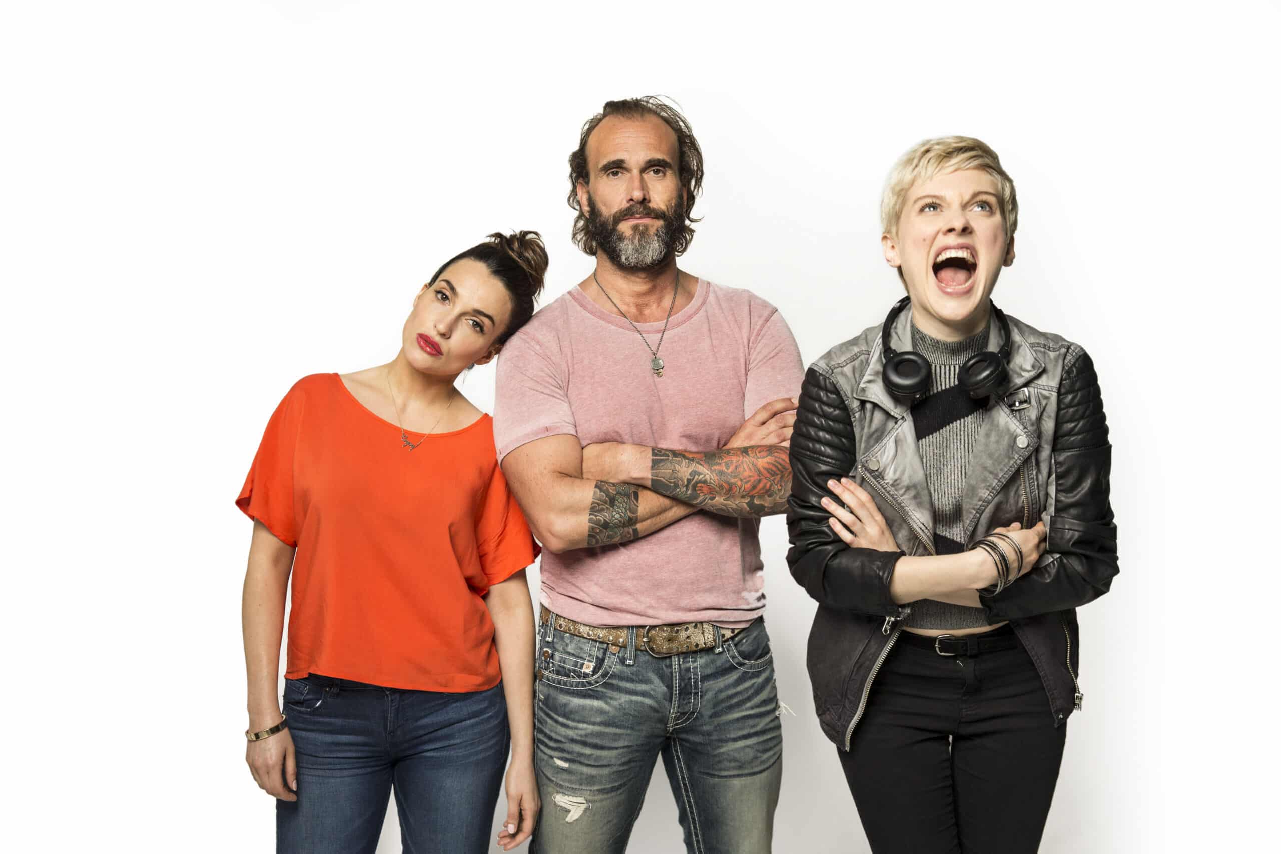 Eine Frau im roten Shirt lehnt sich nach links, ein Mann mit Tattoos und Bart steht mit verschränkten Armen in einem rosa Shirt da und eine Frau in Lederjacke und Kopfhörern mit kurzen blonden Haaren lacht mit offenem Mund vor einem schlichten weißen Hintergrund. © Fotografie Tomas Rodriguez