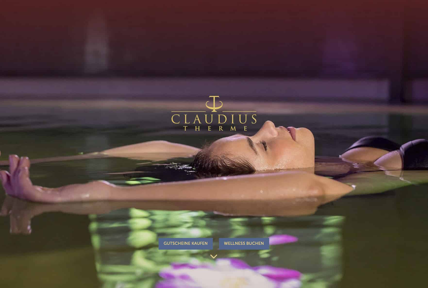 Frau schwimmt mit geschlossenen Augen im Wasser der Claudius Therme. Die ruhige Umgebung ist gedämpft beleuchtet und oben ist das Logo der Therme zu sehen. Unten werden Optionen zum Kauf von Geschenkgutscheinen und zur Buchung von Wellnessanwendungen angezeigt. © Fotografie Tomas Rodriguez