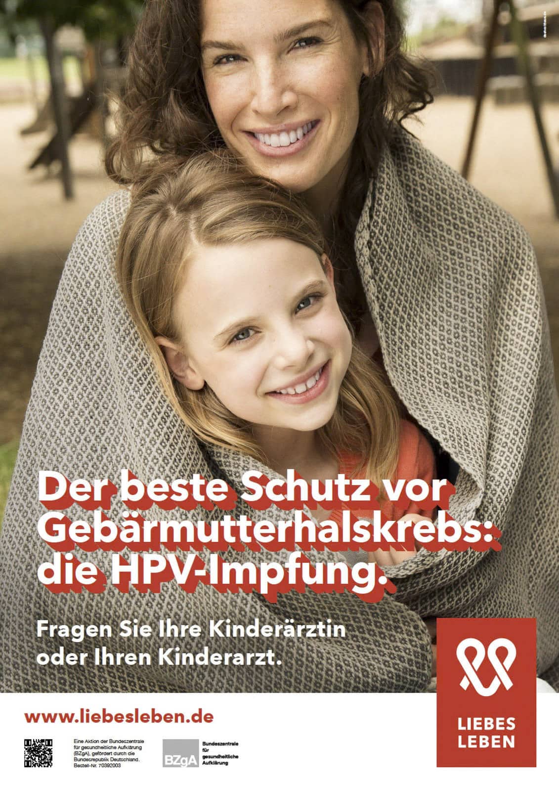 Ein lächelnder Erwachsener und ein Kind sind in eine graue gewebte Decke gehüllt. Der Text wirbt für die HPV-Impfung als besten Schutz gegen Gebärmutterhalskrebs. Das Logo von „LIEBES LEBEN“ und ein Website-Link sind sichtbar. © Fotografie Tomas Rodriguez