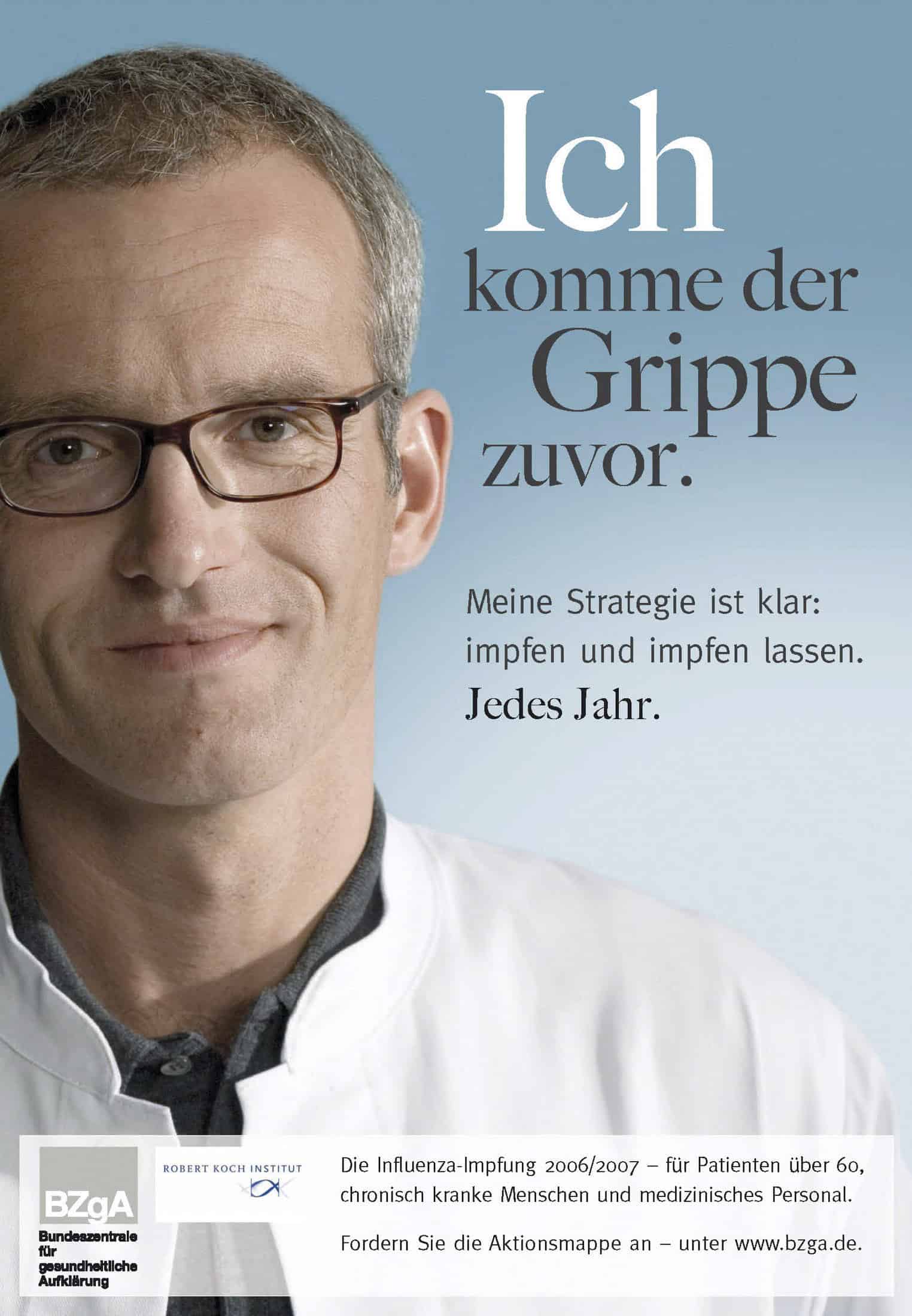 Ein Mann im weißen Kittel steht vor einem Plakat mit der Aufschrift „Ich komme der Grippe zuvor“, das für die Grippeimpfung wirbt. Der Text betont die jährliche Impfung für Patienten über 60, chronisch Kranke und medizinisches Personal. Deutsche Gesundheitsorganisationen werden erwähnt. © Fotografie Tomas Rodriguez