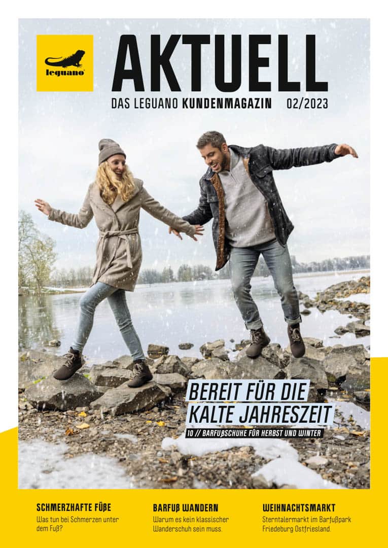 Ein Pärchen tanzt fröhlich auf Felsen an einem See, in Winterkleidung gekleidet. Um sie herum fällt Schnee. Der Covertext lautet „Aktuell“ und beschäftigt sich mit Barfußschuhen für Herbst und Winter, schmerzenden Füßen und einem Weihnachtsmarkt. © Fotografie Tomas Rodriguez