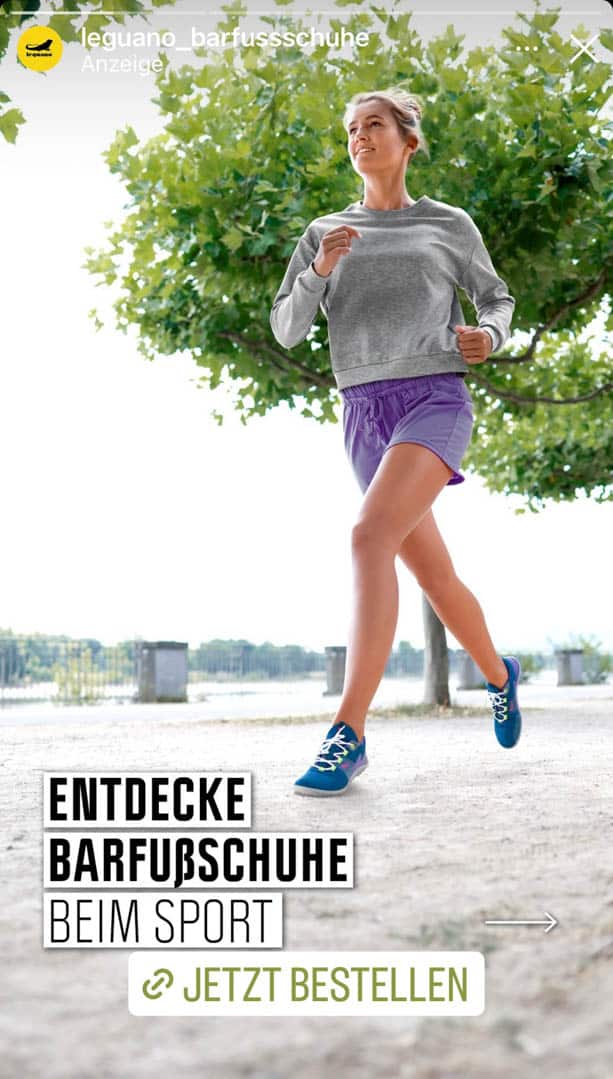 Eine Person mit kurzen Haaren joggt auf einem Kiesweg und trägt ein graues Sweatshirt, lila Shorts und blaue Schuhe. Sie sind im Freien mit grünen Bäumen im Hintergrund. Der Text lautet: „Entdecke Barfußschuhe beim Sport – Jetzt bestellen.“. © Fotografie Tomas Rodriguez