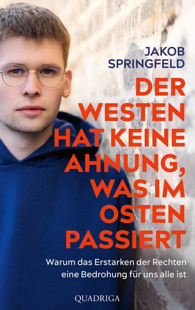 Eine Person in einem blauen Kapuzenpullover steht vor einer beigen Wand. Der Text lautet: „Jakob Springfield. Der Westen hat keine Ahnung, was im Osten passiert. Warum das Erstarken der Rechten eine Bedrohung für uns alle ist.“. © Fotografie Tomas Rodriguez