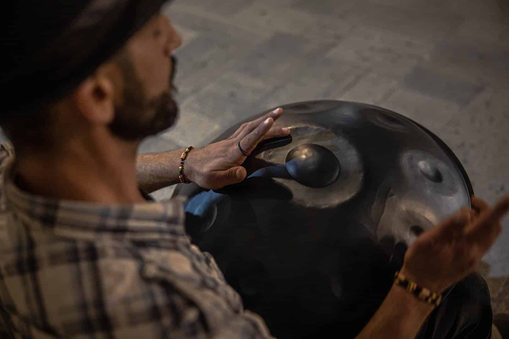 Ein Mann mit kariertem Hemd und Hut spielt mit seinen Händen eine Hängetrommel. Das Bild ist von oberhalb seiner Schulter aufgenommen und konzentriert sich auf seine Hände und das Instrument. © Fotografie Tomas Rodriguez