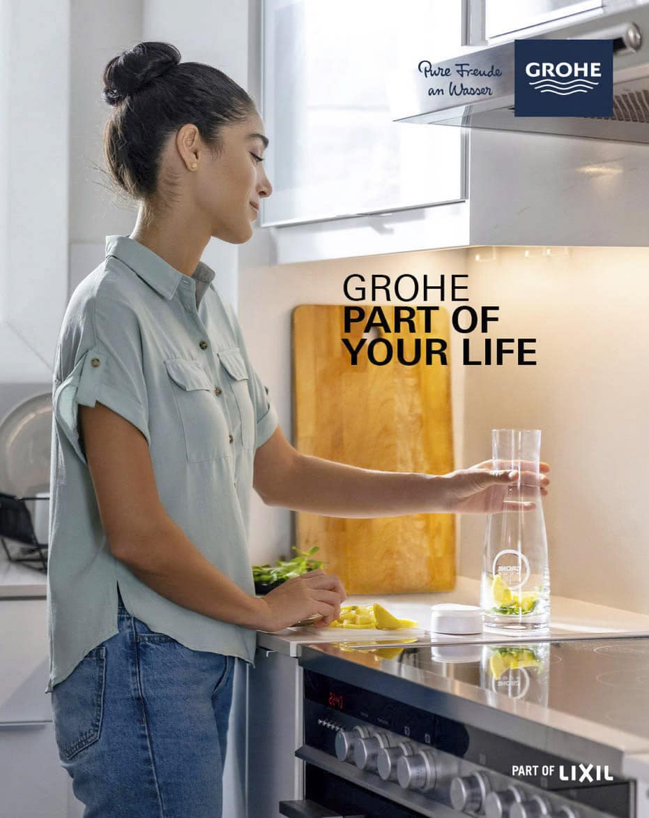 Eine Frau in einem hellgrünen Hemd gießt Wasser aus einem GROHE Wasserhahn in einen Glaskrug mit Zitronenscheiben in einer modernen Küche. Der Text lautet "GROHE PART OF YOUR LIFE" und enthält GROHE- und LIXIL-Logos. © Fotografie Tomas Rodriguez