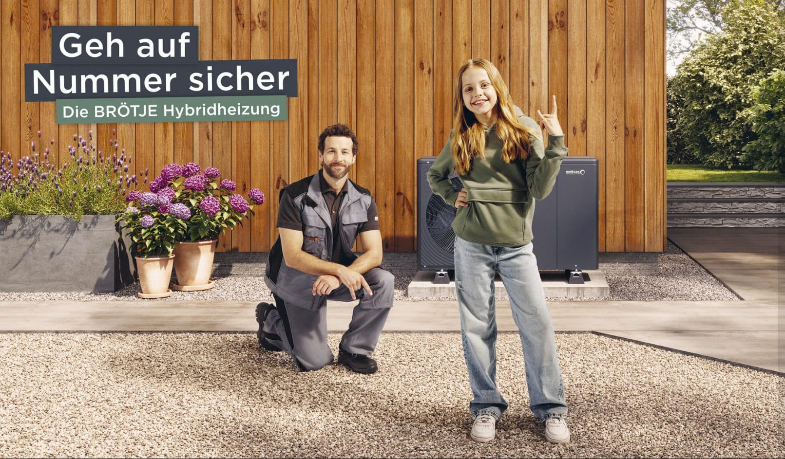 Ein lächelndes junges Mädchen steht mit einem Friedenszeichen neben einem knienden Techniker vor einem modernen Holzhaus, mit Pflanzen und BRÖTJE-Hybridheizgeräten im Hintergrund. Oben links erscheint ein Text in deutscher Sprache. © Fotografie Tomas Rodriguez