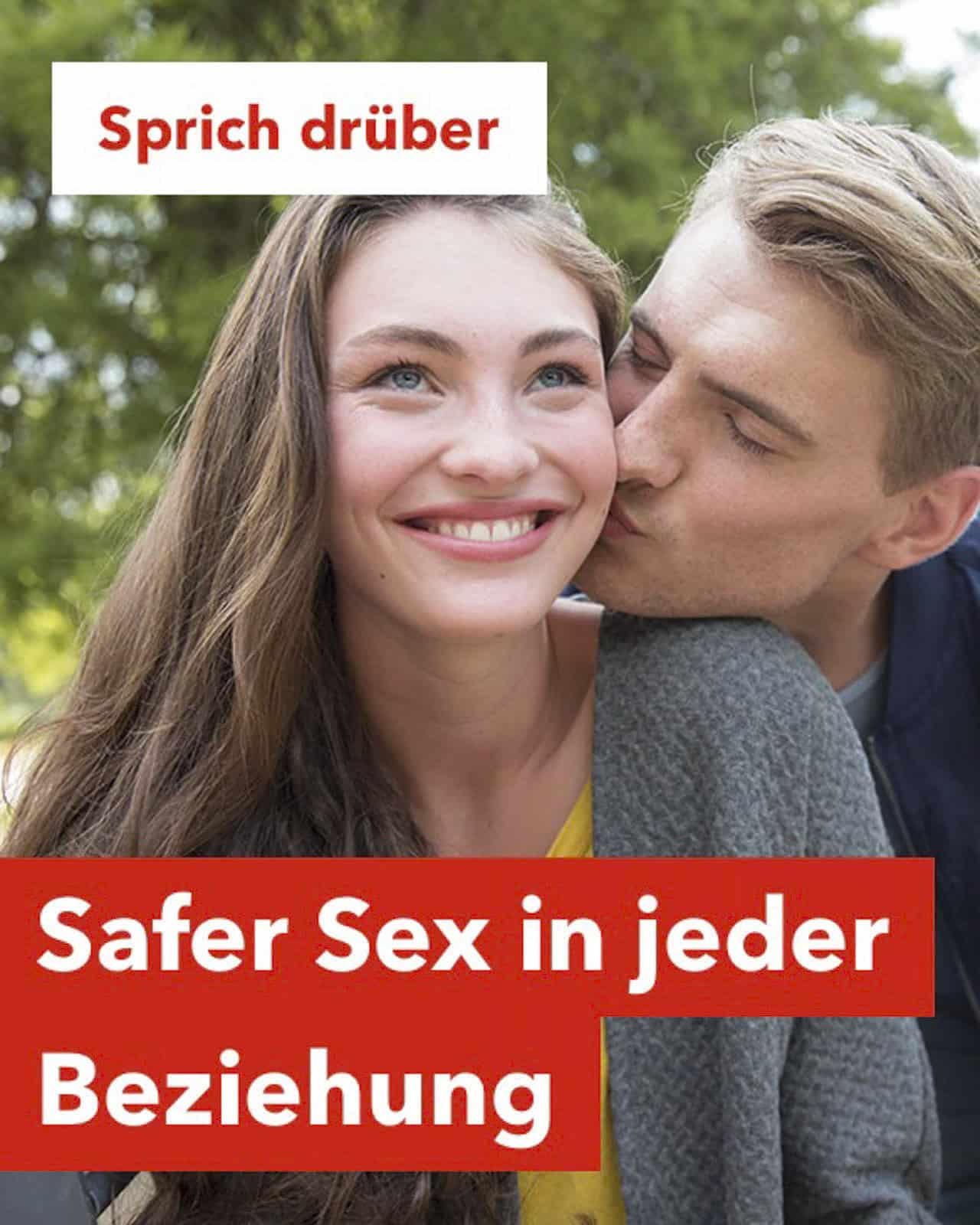Eine lächelnde Frau wird von einem Mann im Freien umarmt und auf die Wange geküsst. Der deutsche Text lautet "Sprich drüber" und "Safer Sex in jeder Beziehung" und wirbt für die Kommunikation über Safer Sex in allen Beziehungen. © Fotografie Tomas Rodriguez