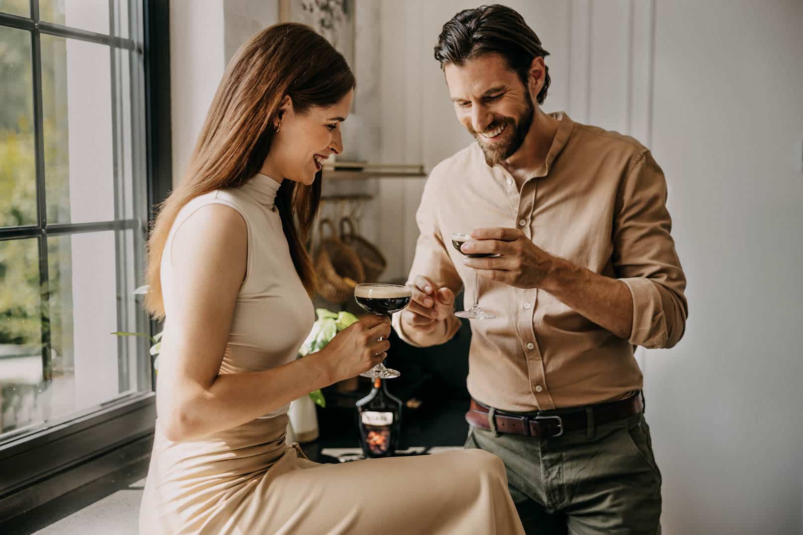 Ein lächelnder Mann und eine lächelnde Frau genießen gemeinsam Espresso-Martinis in einer hellen, modernen Küche. Die Frau sitzt auf dem Tresen, und der Mann steht neben ihr, beide lachen und halten Cocktailgläser in der Hand. © Fotografie Tomas Rodriguez