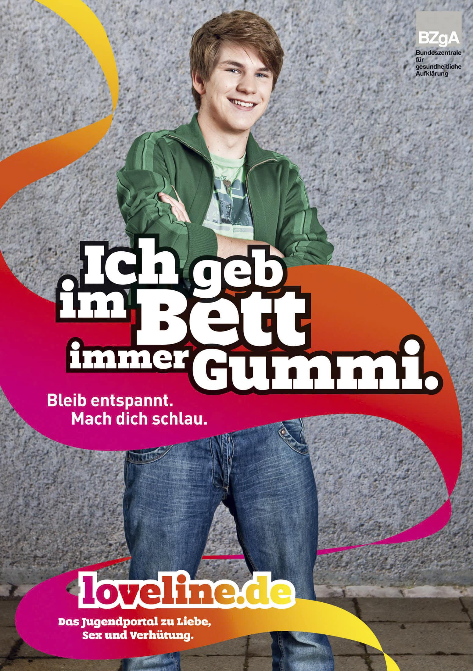Ein lächelnder junger Mann in einer grünen Jacke steht mit verschränkten Armen vor einer grauen Wand. Über ihm steht in fetter Schrift auf Deutsch: "Ich geb im Bett immer Gummi." Darunter befindet sich ein rosa Kasten mit Safer-Sex-Ratschlägen und einem Logo für loveline.de. © Fotografie Tomas Rodriguez