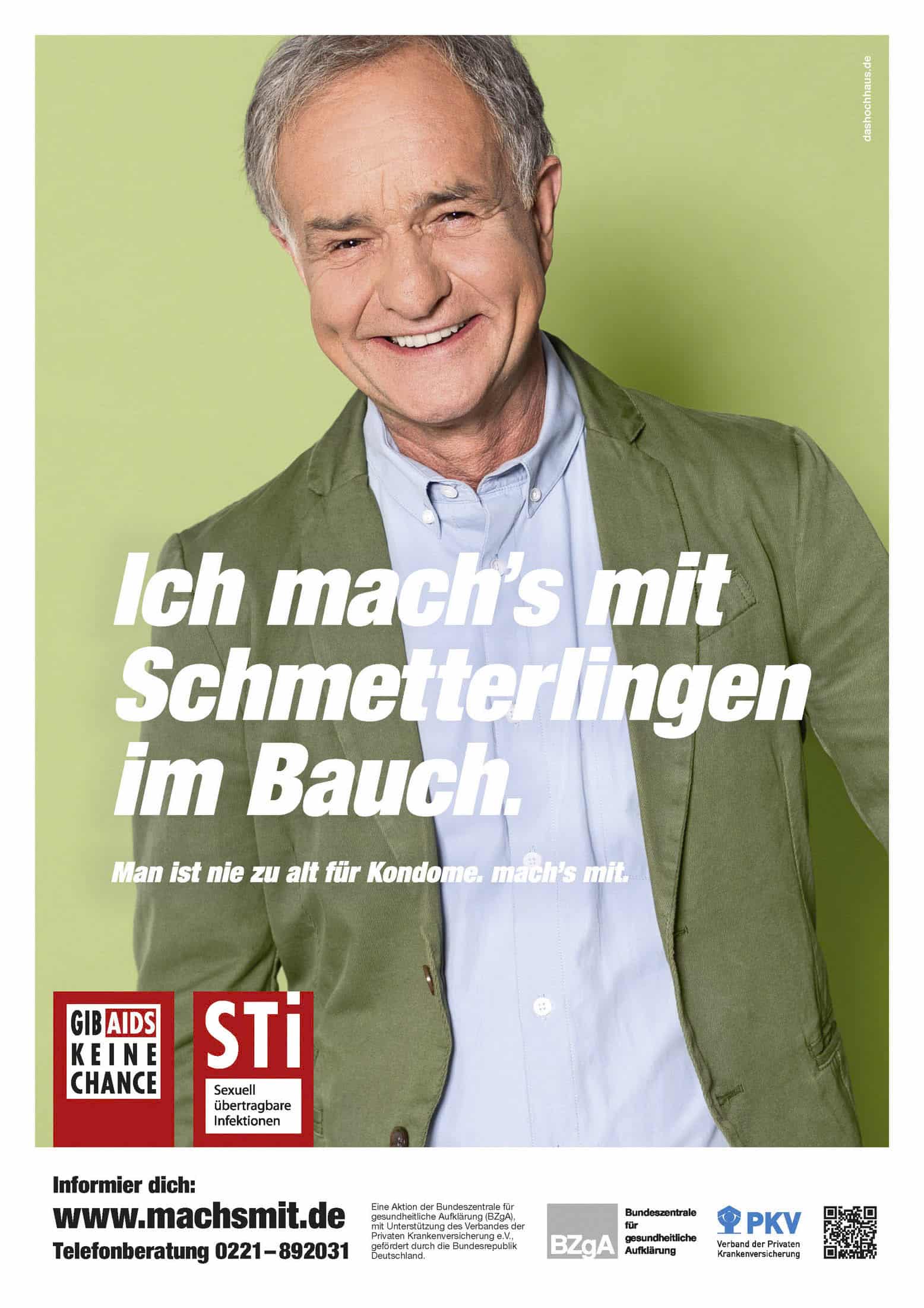 Ein älterer Mann in grüner Jacke und blauem Hemd steht vor einem hellen Hintergrund und lächelt selbstbewusst. Ein großer deutscher Text wirbt für die Verwendung von Kondomen und das Bewusstsein für sexuelle Gesundheit, darunter befinden sich Informationslogos und Kontaktangaben. © Fotografie Tomas Rodriguez